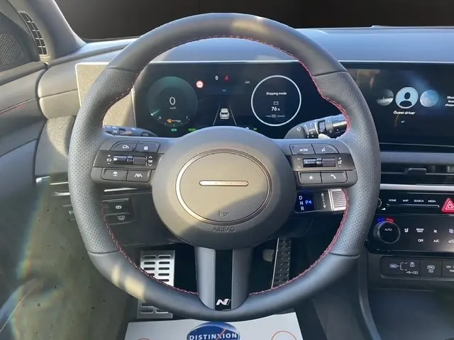 Vue centrée sur le volant cuir noir avec surpiqûres rouges du Hyundai Tucson 1.6 Hybrid 2026, tableau de bord numérique visible.