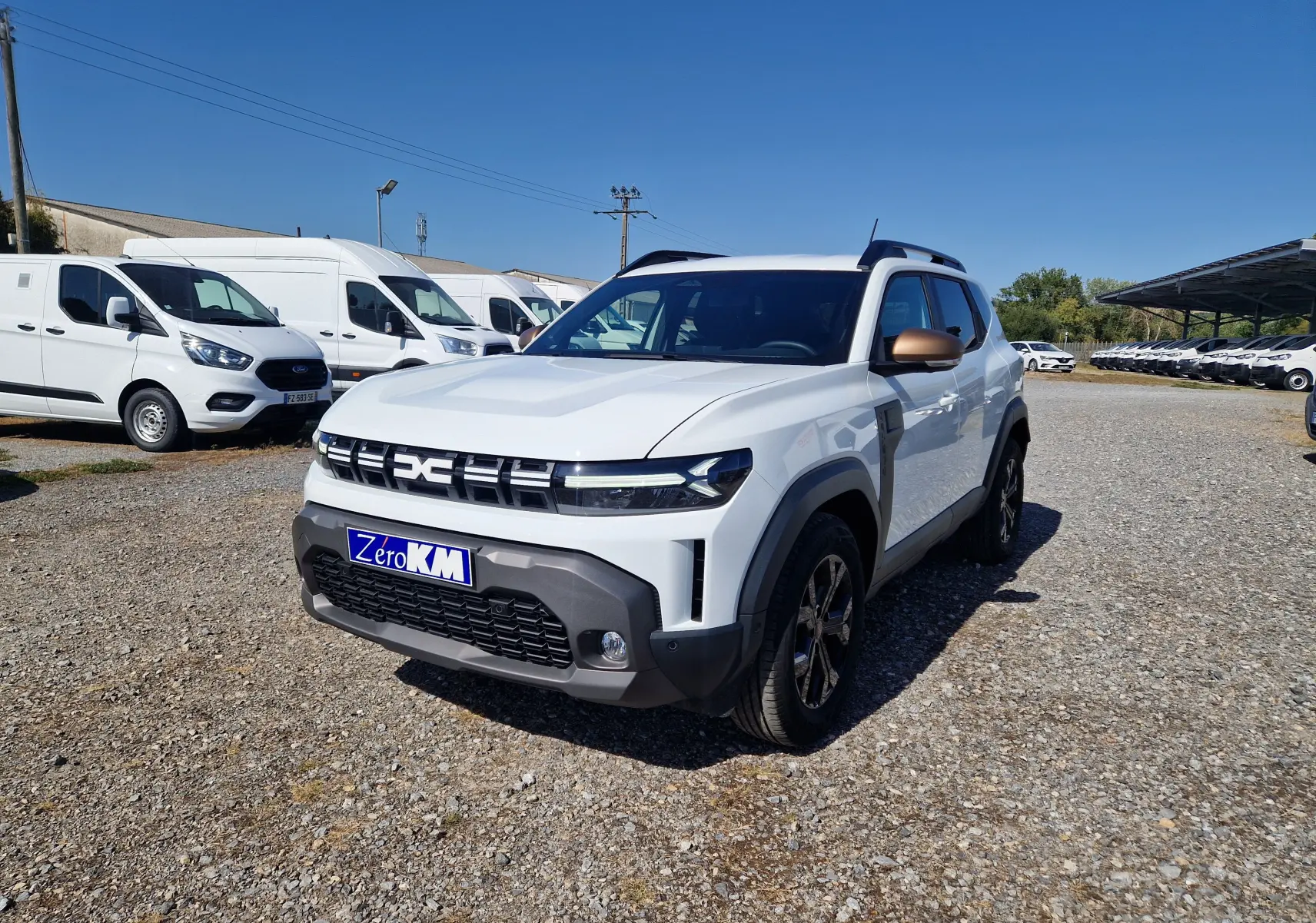 Vue 3/4 avant droite du Dacia Duster blanc 2026 avec rétroviseurs bronze et calandre noire distinctive.