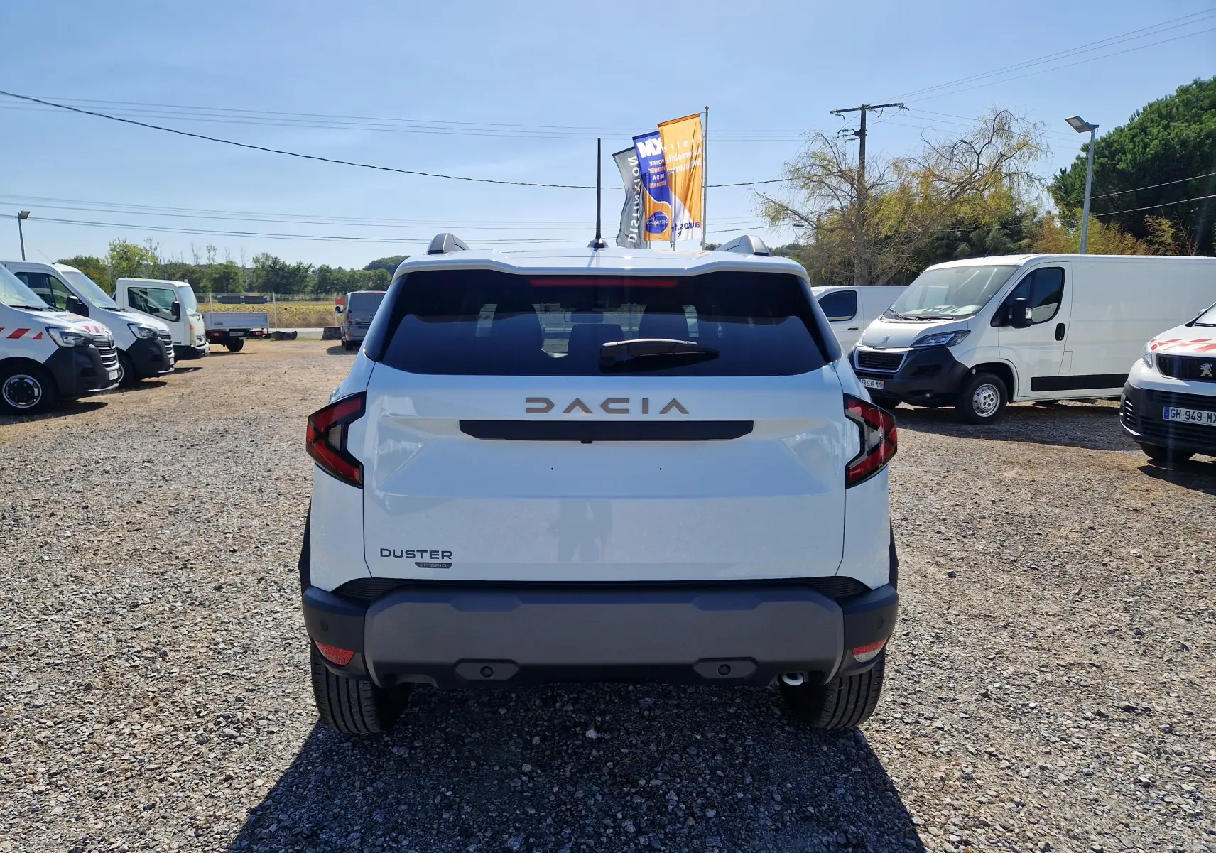 Vue arrière d'un Dacia Duster blanc 2026 hybride, avec logo DACIA en relief et feux arrière anguleux, stationné en extérieur.