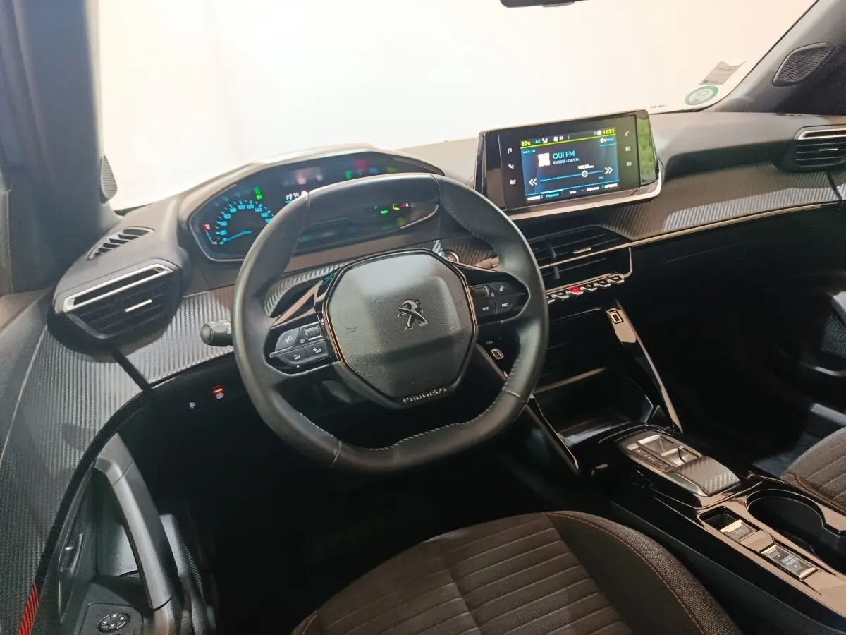 Vue intérieure du tableau de bord et volant cuir noir du Peugeot E-2008 électrique avec écran tactile central allumé.