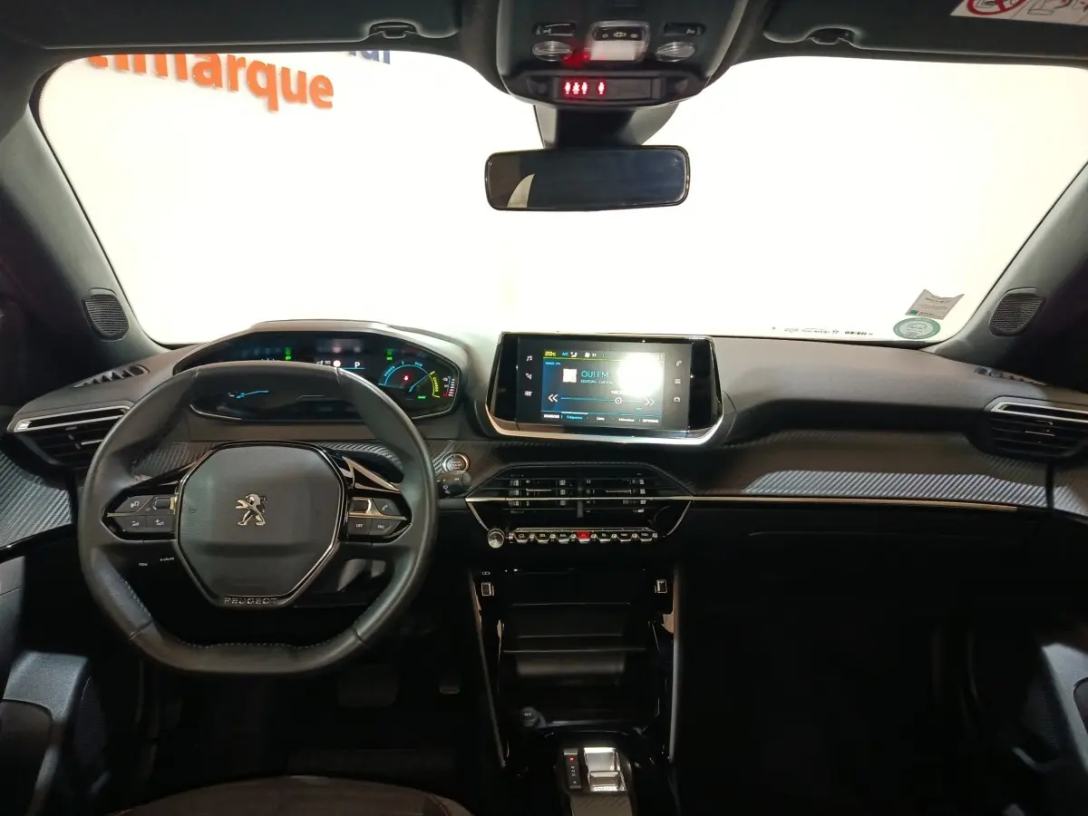 Vue intérieure frontale du tableau de bord et volant cuir noir du Peugeot E-2008 électrique gris clair 2023 avec écran tactile central.