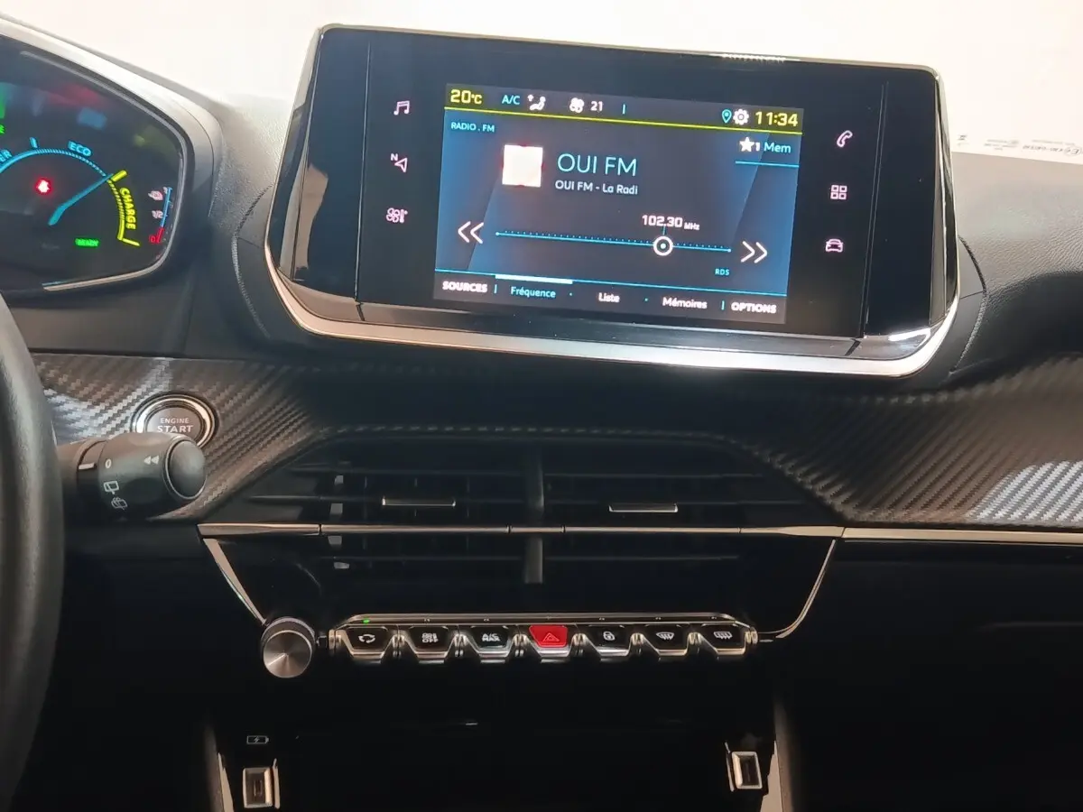 Vue rapprochée du tableau de bord de la Peugeot E-2008 électrique 2023 avec écran tactile central allumé et finition carbone.