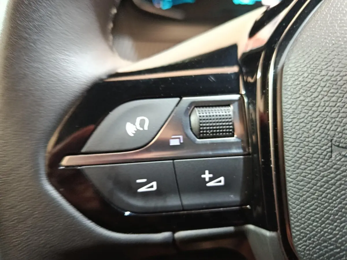Gros plan sur les commandes de volume et de fonction vocale au volant cuir noir d'une Peugeot E-2008 électrique 2023.