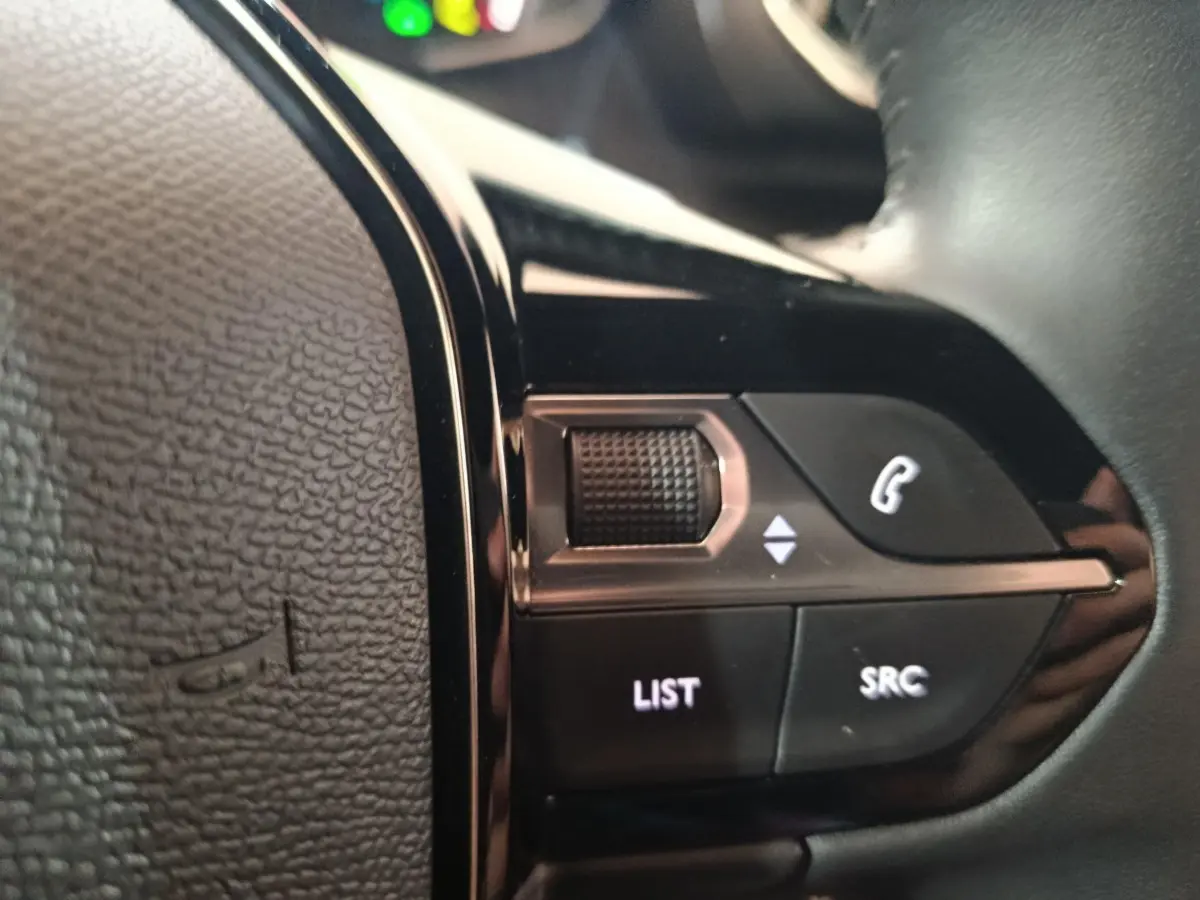 Gros plan sur les commandes multifonctions noires du volant cuir de la Peugeot E-2008 électrique gris clair.
