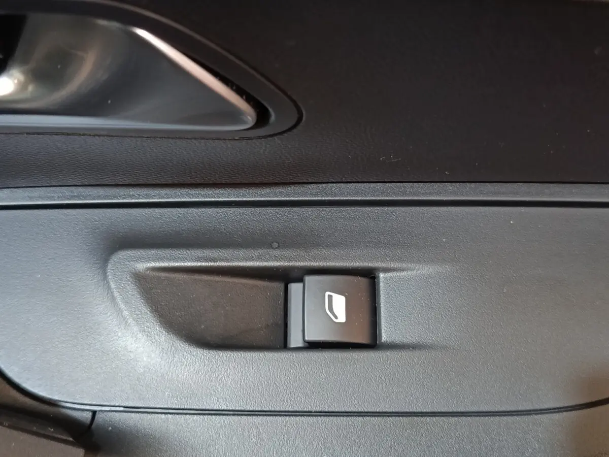 Gros plan sur le bouton de commande de lève-vitre côté conducteur de la Peugeot E-2008 électrique gris clair 2023.