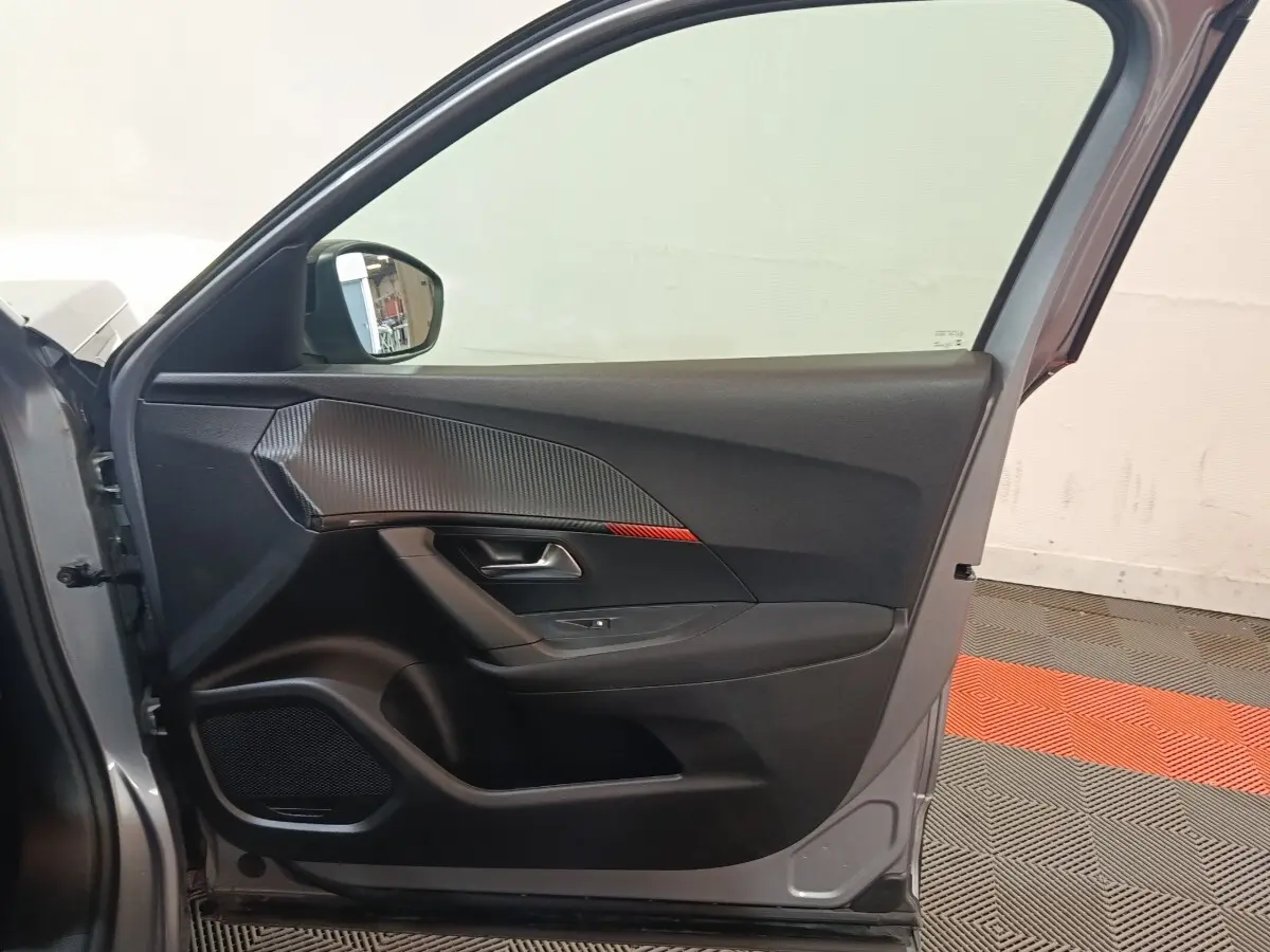 Vue intérieure de la porte avant gauche gris clair du Peugeot E-2008 électrique avec insert décoratif noir et rouge.
