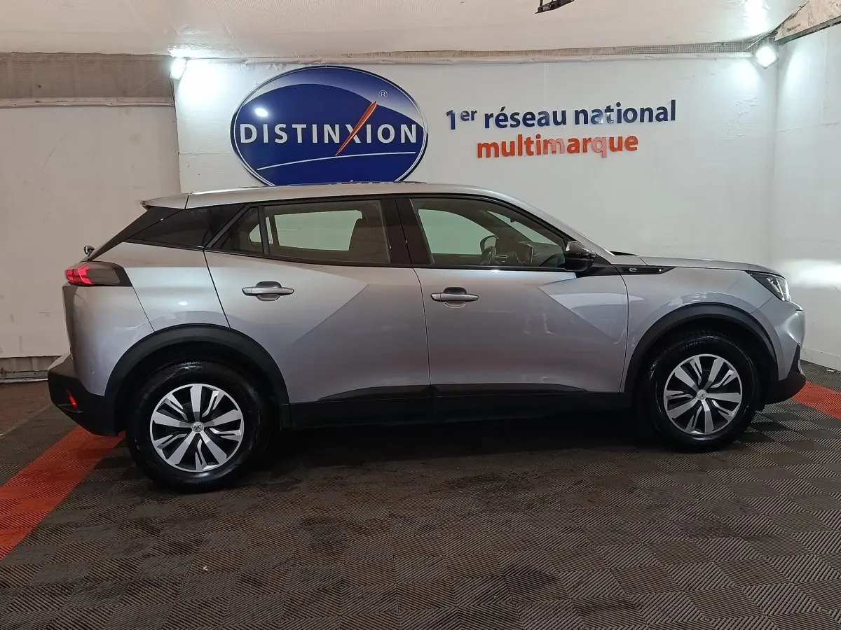 Profil droit d'un Peugeot E-2008 électrique gris clair 2023 avec jantes alliage et toit noir contrasté.
