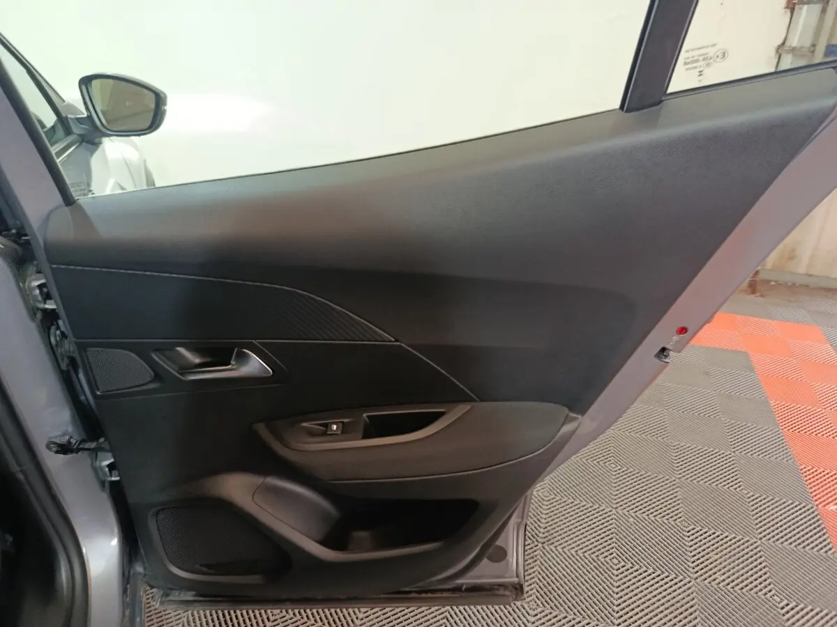 Vue intérieure de la porte arrière gauche gris clair du Peugeot E-2008 électrique 2023, avec poignée et commande de vitre.