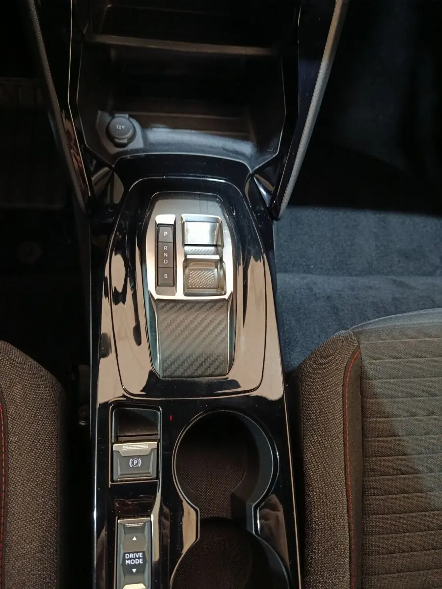 Vue plongeante sur la console centrale noire brillante du Peugeot E-2008 électrique avec sélecteur de vitesse et porte-gobelets.