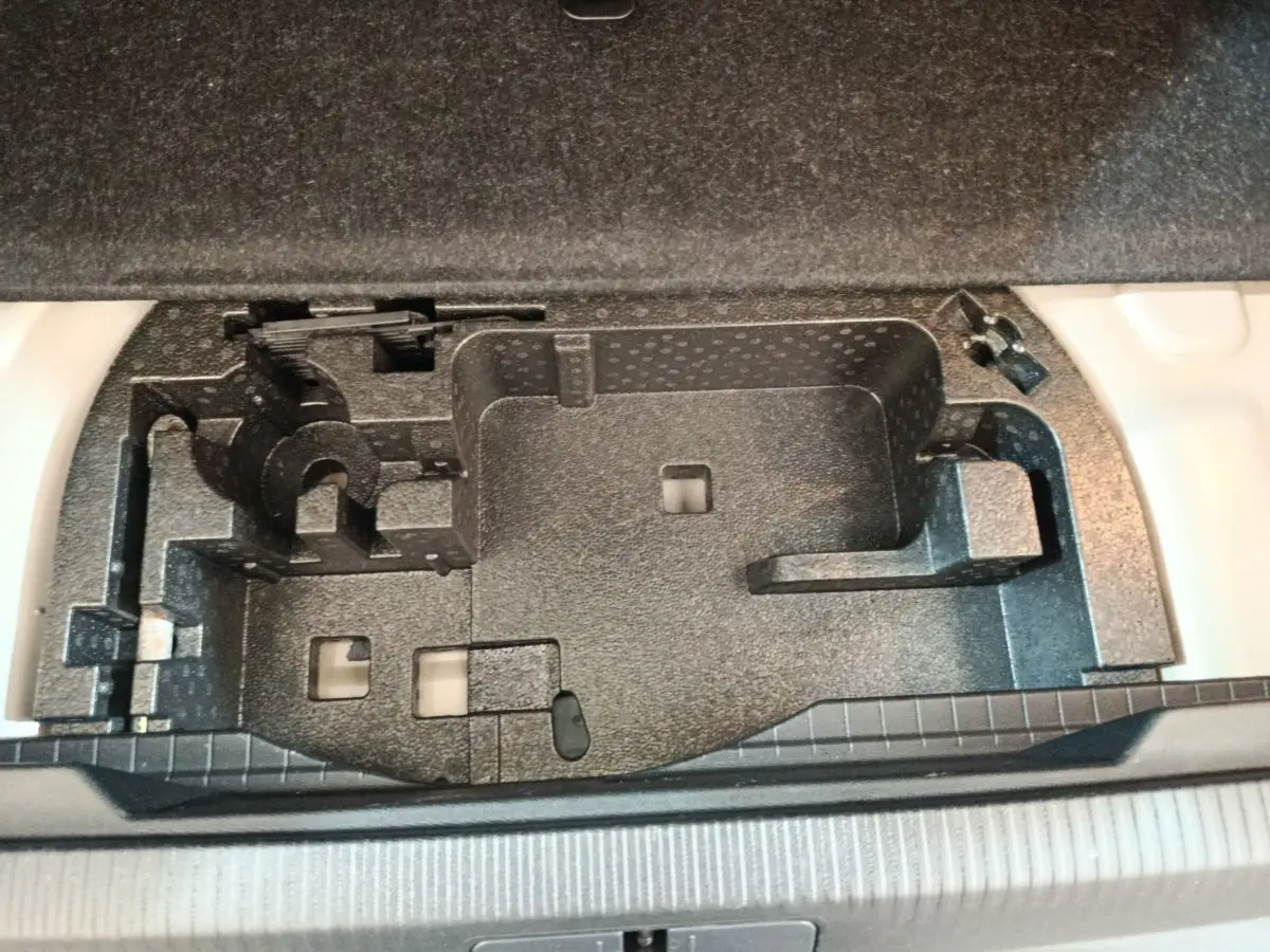 Compartiment de rangement noir sous le plancher du coffre du Peugeot E-2008 électrique gris clair, vue plongeante.