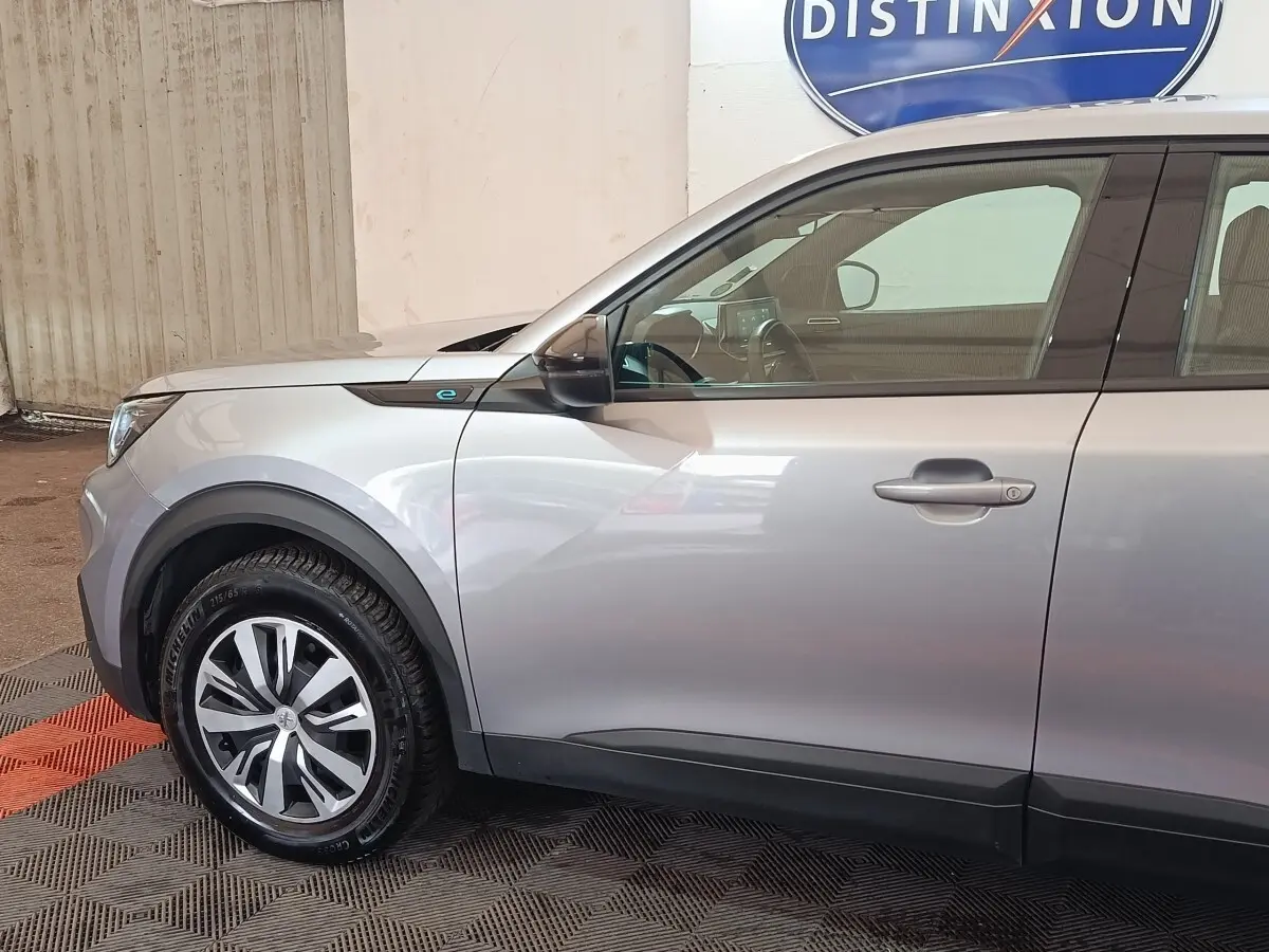 Vue de profil côté gauche du Peugeot E-2008 électrique gris clair, mettant en valeur la jante et le badge "e" près de l'aile avant.