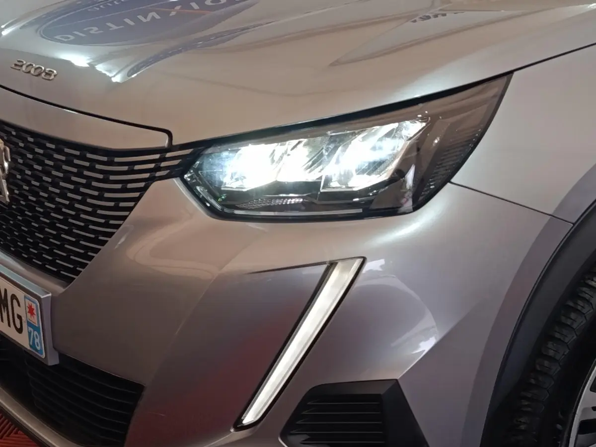 Gros plan sur l'avant droit gris clair du Peugeot E-2008 électrique 2023, avec phare LED allumé et calandre noire.