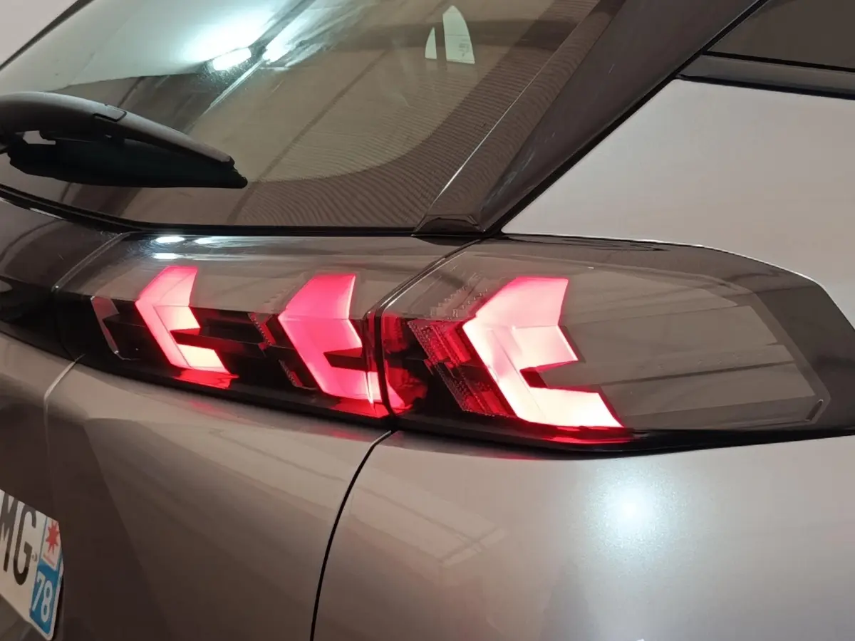 Gros plan sur le feu arrière droit rouge allumé du Peugeot E-2008 électrique gris clair 2023.