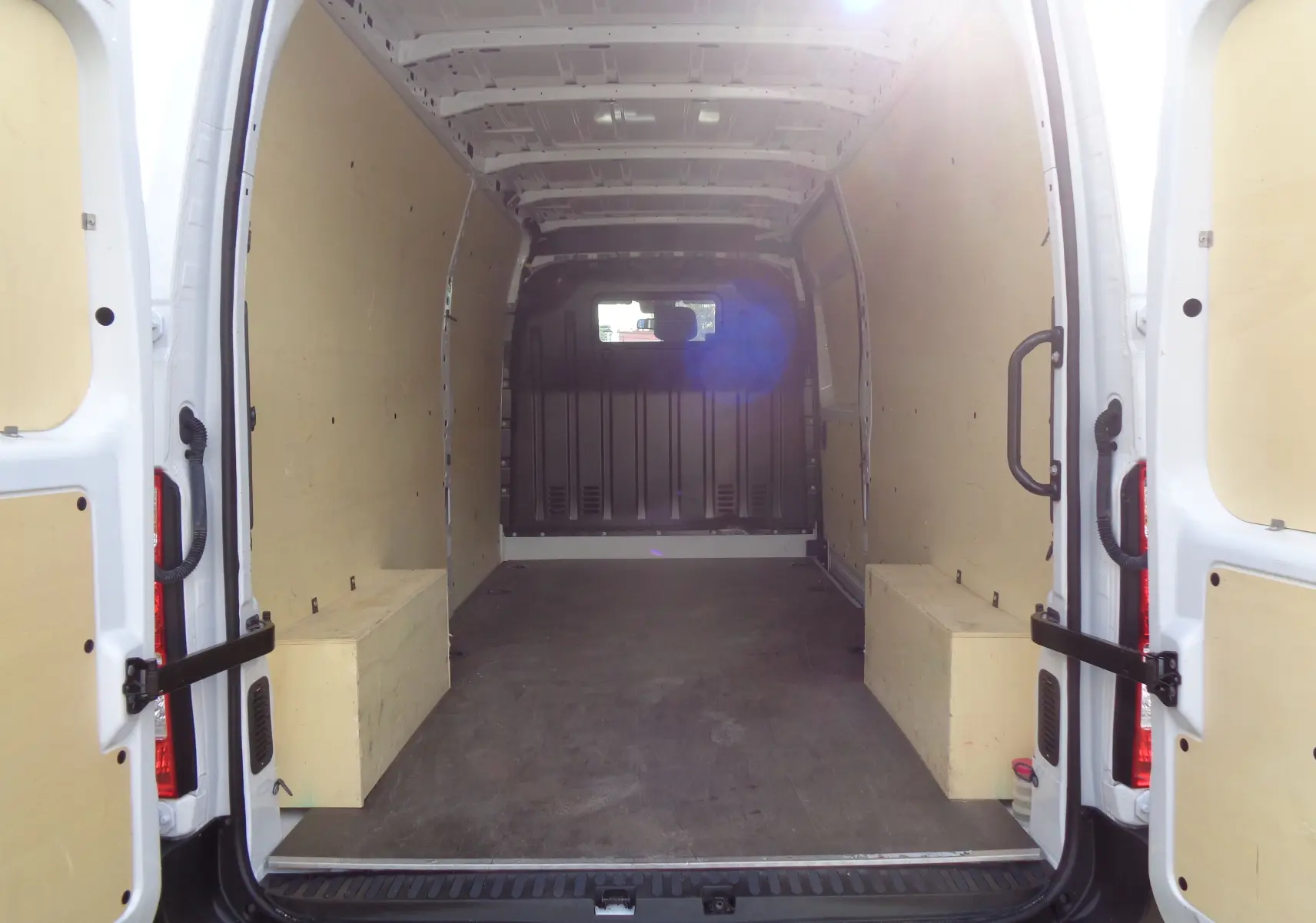 Intérieur vide vu de l'arrière d'un Opel Movano Fourgon blanc polaire, avec parois et plancher protégés en bois clair.
