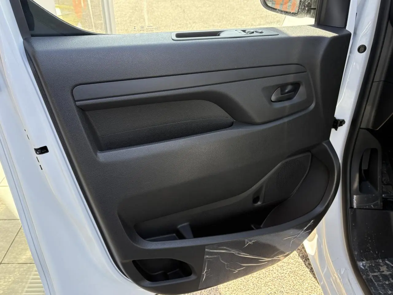 Vue de la porte avant droite ouverte d'un Opel Vivaro blanc, montrant le panneau intérieur noir avec rangement intégré.