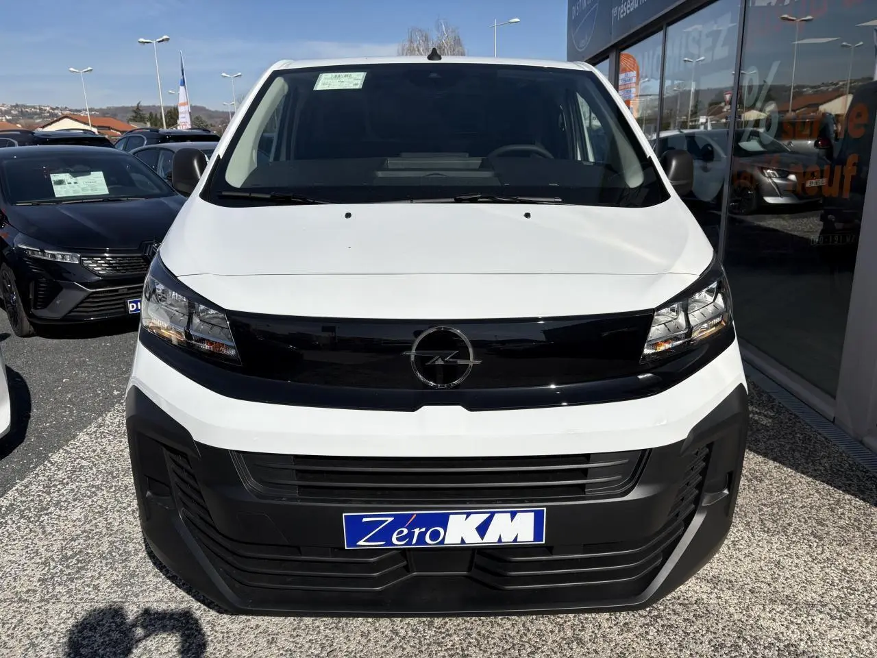 Vue frontale d'un Opel Vivaro blanc avec calandre noire brillante et plaque Zéro KM visible.