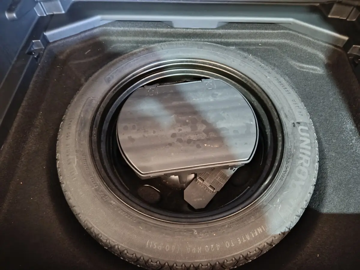 Gros plan sur la roue de secours dans le coffre d'un Peugeot 3008 blanc, avec rangement d'outils visible.