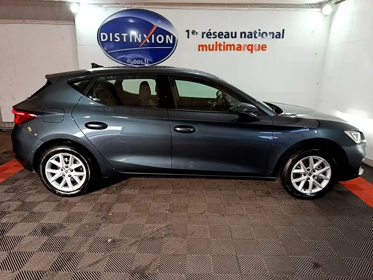 Vue de profil côté gauche d'une SEAT Leon gris clair 2023, avec jantes alliage et feux arrière LED visibles.