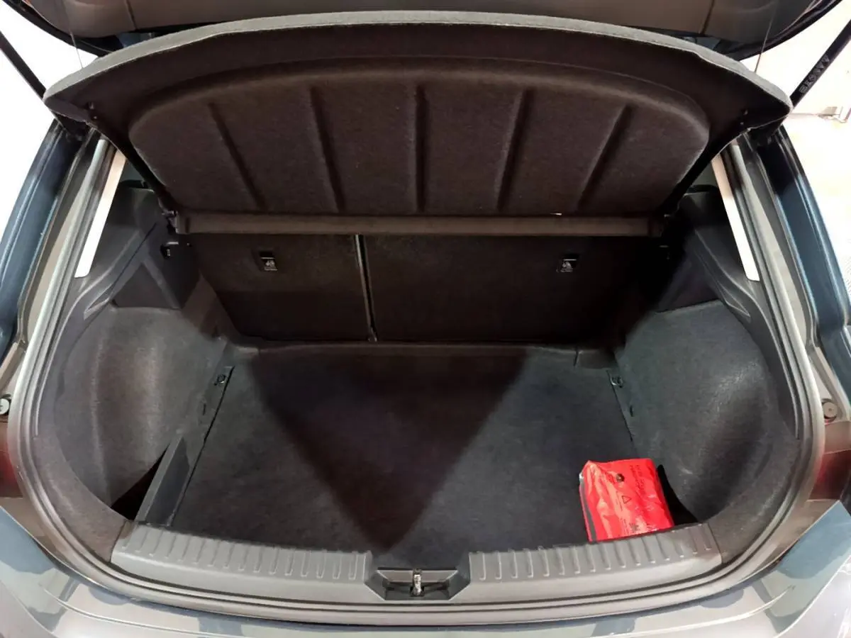 Vue arrière du coffre ouvert d'une SEAT Leon gris clair 2023, avec banquette rabattable et trousse de secours rouge visible.