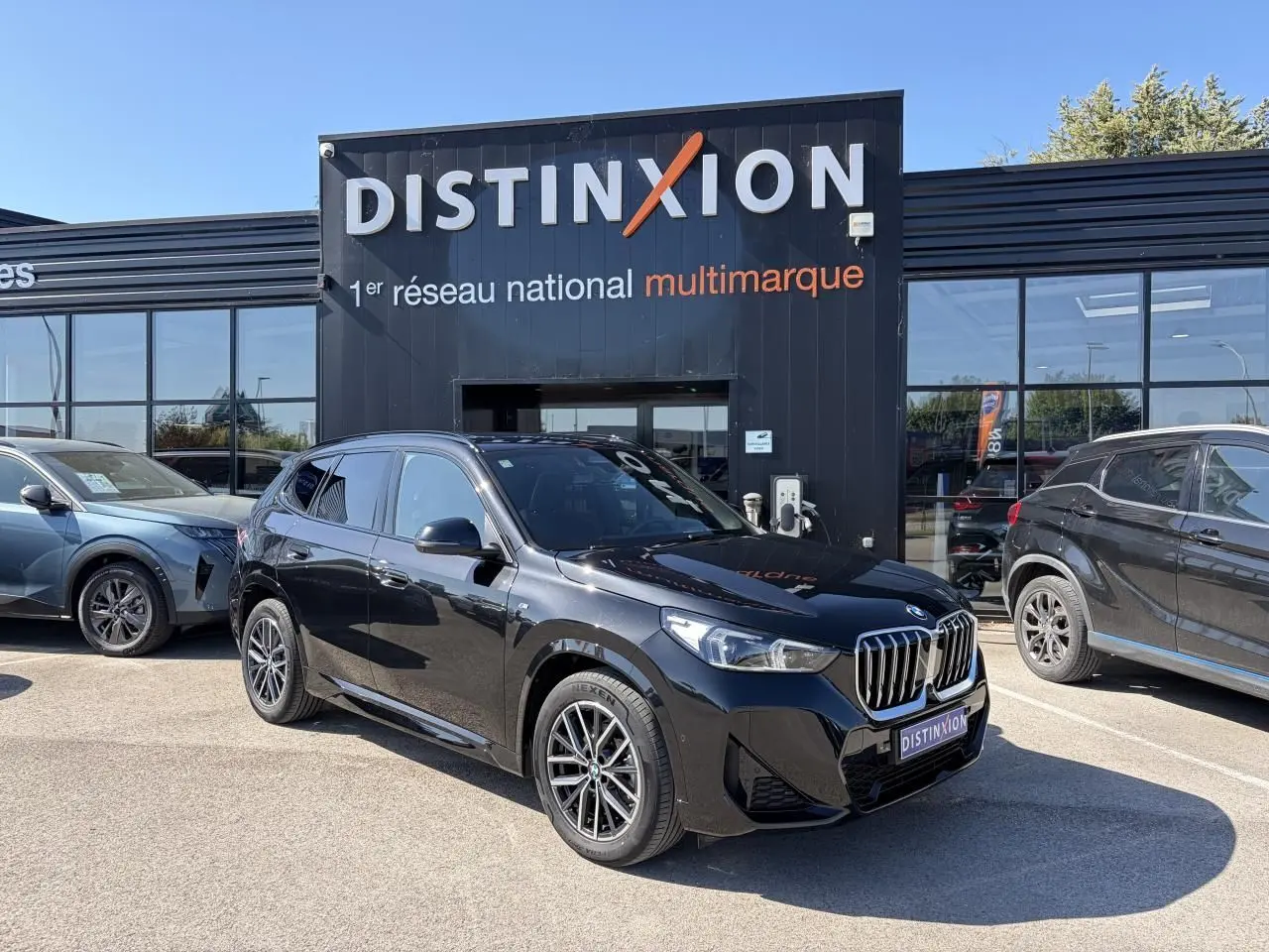 BMW X1 noir saphir vue 3/4 avant droit, avec calandre chromée et jantes alliage 18 pouces bicolores.