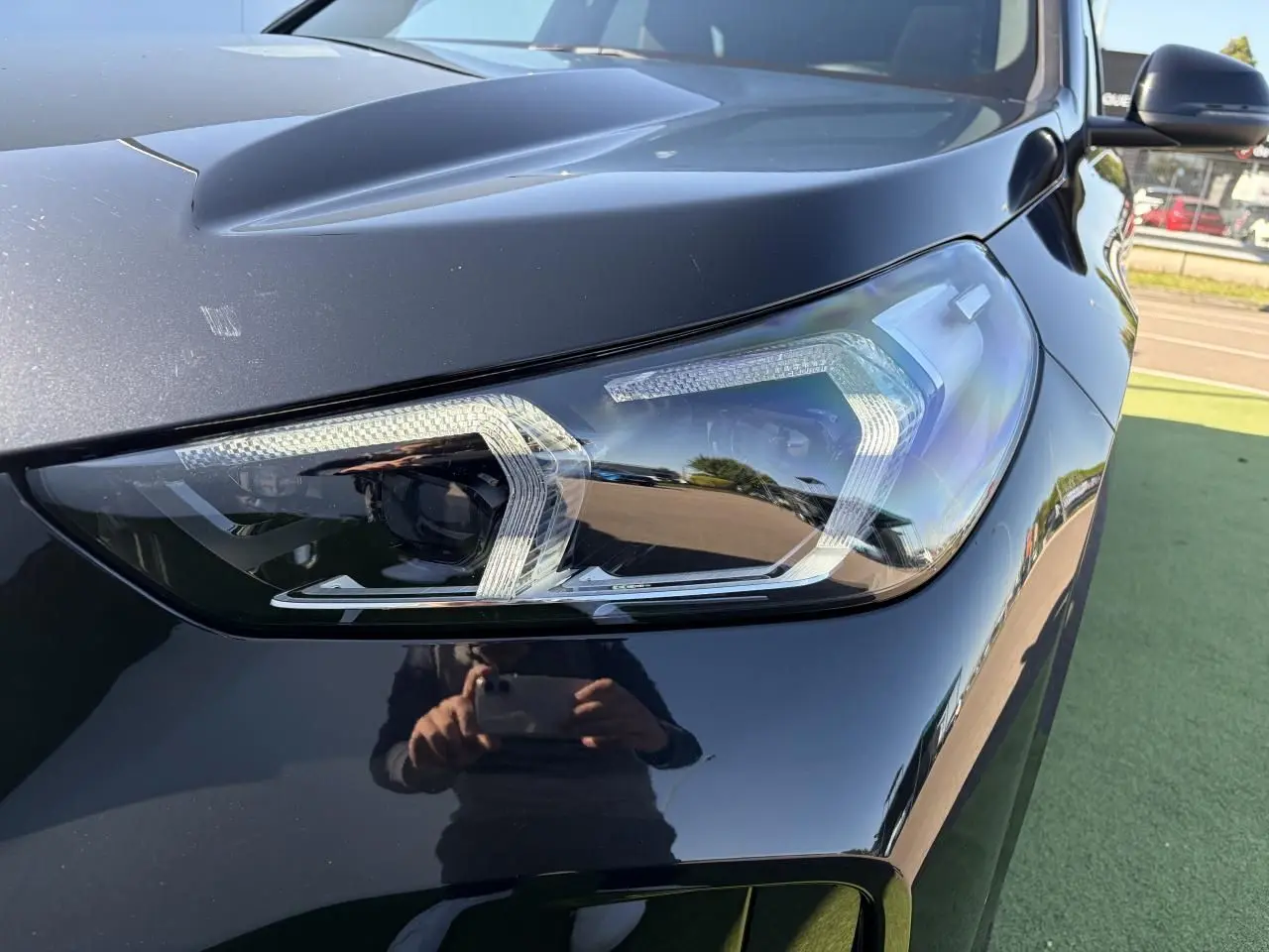 Gros plan sur le phare avant droit d’un BMW X1 noir saphir, mettant en valeur la finition LED et la carrosserie brillante.
