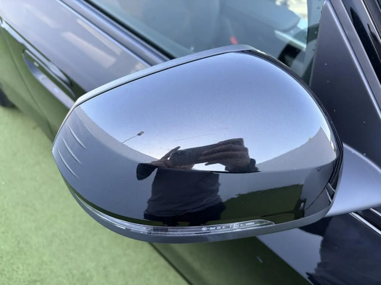 Rétroviseur extérieur droit noir saphir brillant d'une BMW X1 2025, vue rapprochée sur fond vert.