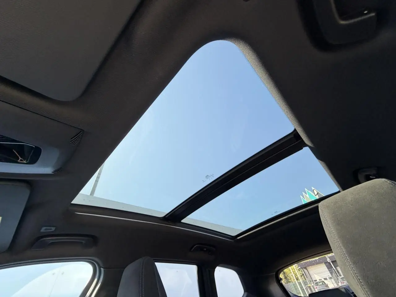 Vue intérieure du toit ouvrant panoramique en verre du BMW X1 noir Saphir, avec ciel bleu visible à travers.