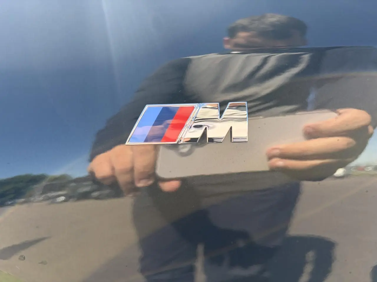 Gros plan sur l'emblème M chromé sur la carrosserie noir saphir brillante d'un BMW X1 2025.