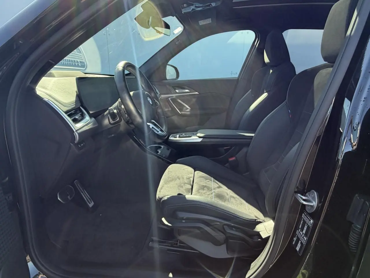 Intérieur côté conducteur de la BMW X1 noir saphir, sièges sport Alcantara avec surpiqûres bleues et tableau de bord moderne.