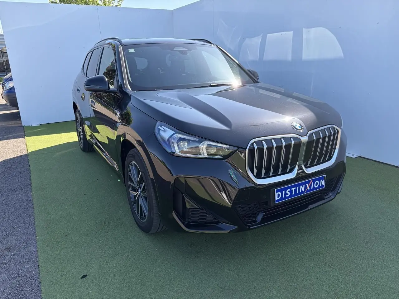 BMW X1 noir saphir vue 3/4 avant droite, avec calandre chromée et jantes alliage 18 pouces visibles.