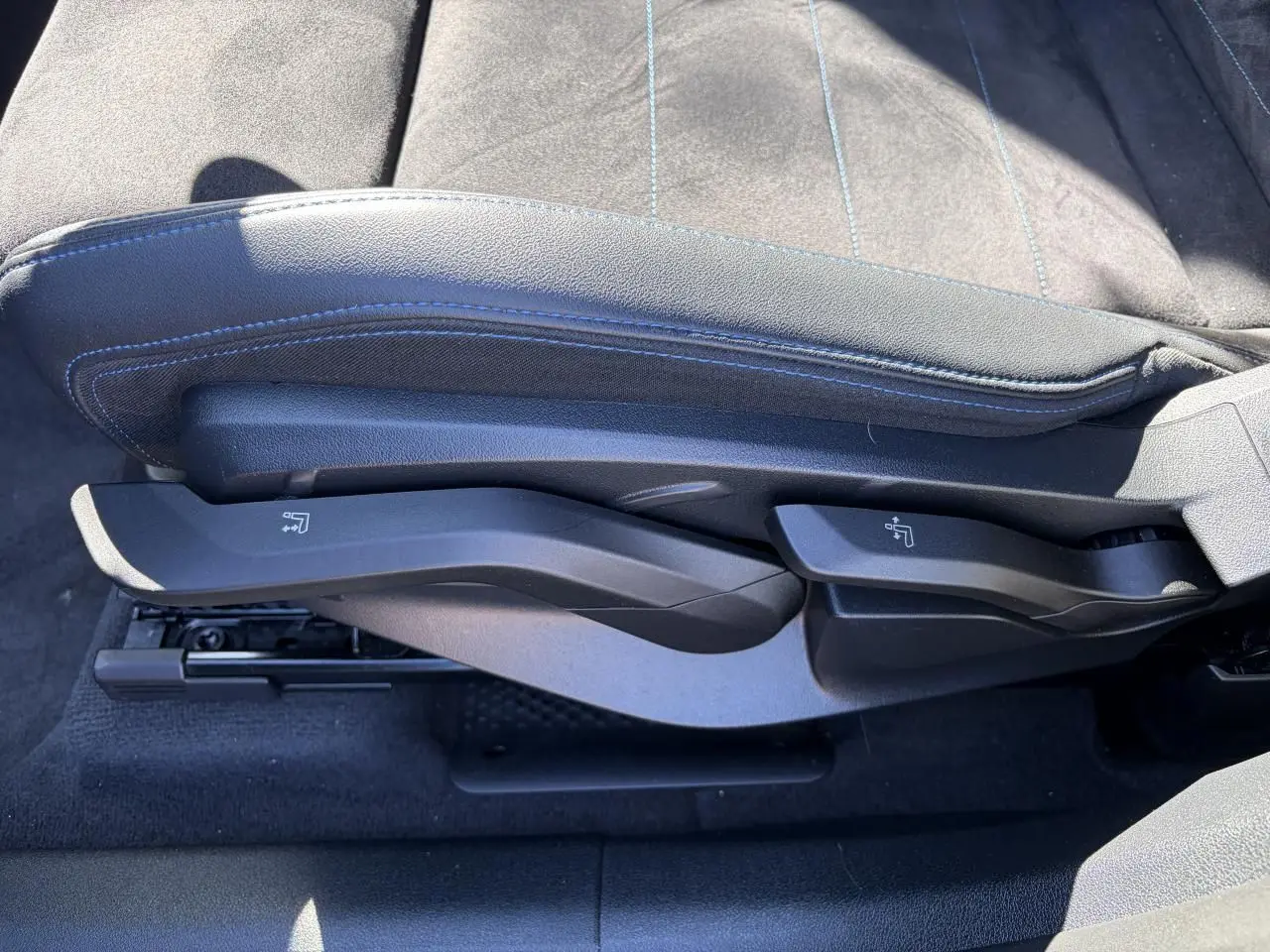 Gros plan sur les commandes latérales du siège avant en Alcantara noir avec surpiqûres bleues du BMW X1 2025.