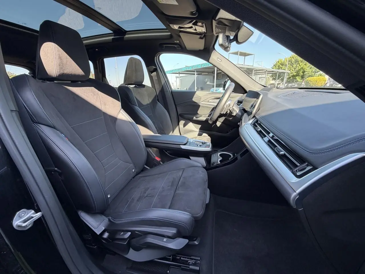 Vue intérieure côté conducteur du BMW X1 2025 avec sièges sport Alcantara noirs et toit ouvrant panoramique.
