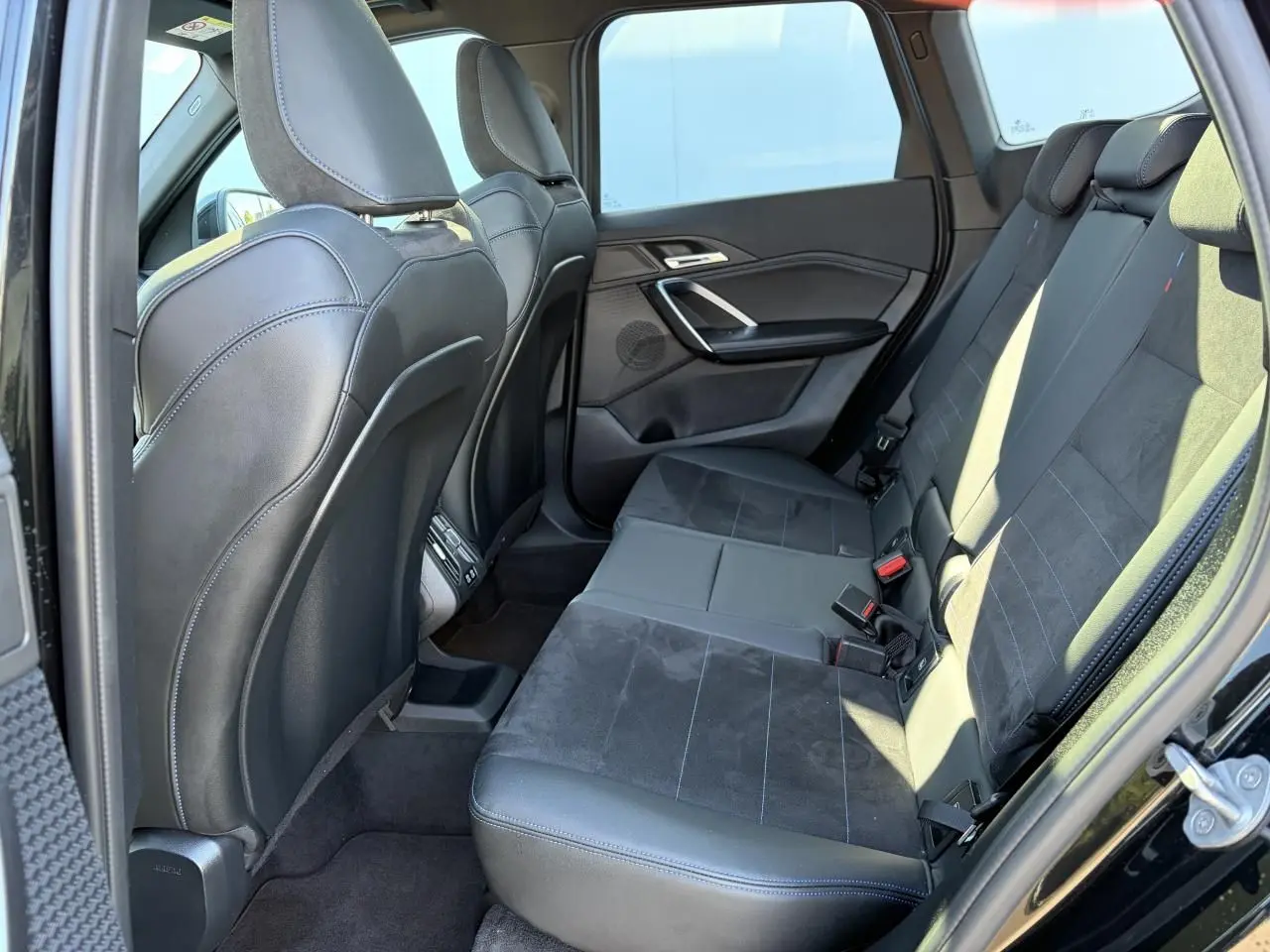 Vue intérieure côté gauche de la banquette arrière en cuir noir avec surpiqûres bleues du BMW X1 2025 noir saphir.