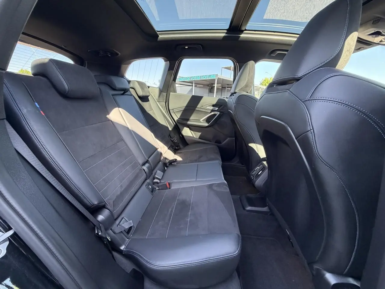 Vue intérieure arrière de la BMW X1 noire avec banquette Alcantara, toit ouvrant panoramique et finitions M Sport.