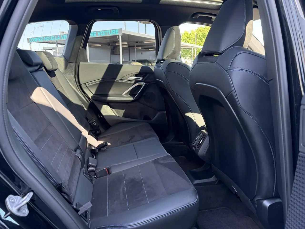 Vue intérieure côté gauche de la banquette arrière en Alcantara noir avec surpiqûres bleues du BMW X1 noir Saphir 2025.
