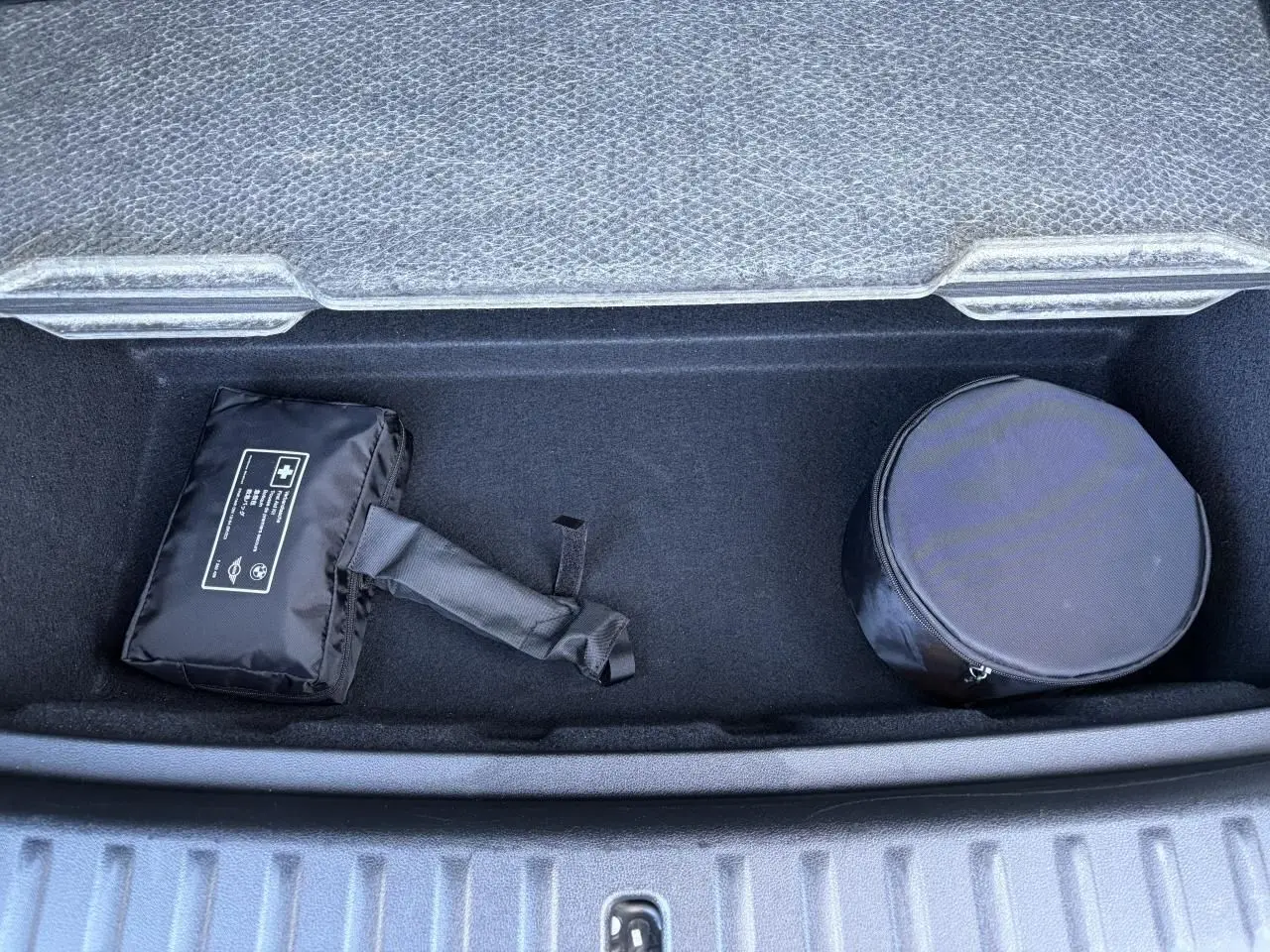 Coffre de BMW X1 noir Saphir 2025 vu de dessus, avec trousse de secours et rangement rond noir.