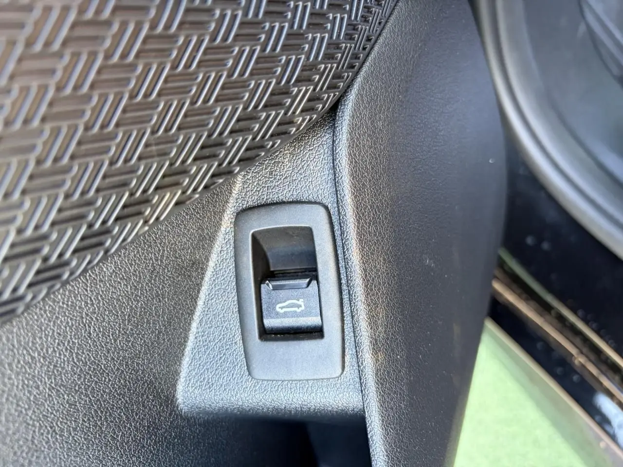 Détail du bouton d'ouverture du coffre sur la portière intérieure d'une BMW X1 noir saphir.