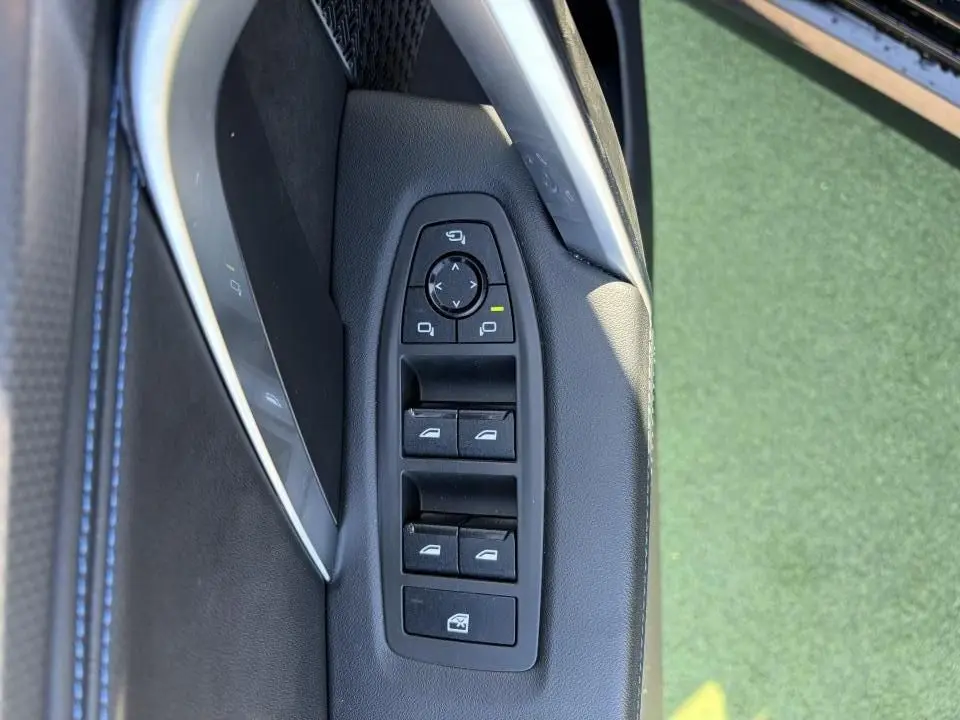 Gros plan sur les commandes de lève-vitres et rétroviseurs côté gauche, intérieur noir avec surpiqûres bleues du BMW X1 noir Saphir.