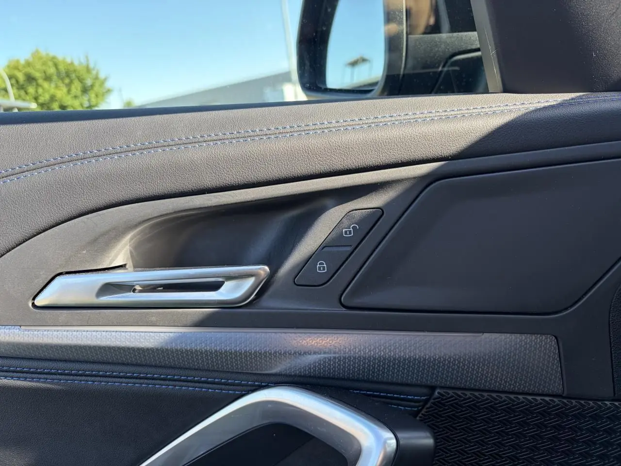 Détail de la porte côté conducteur d’un BMW X1 noir Saphir, montrant la poignée argentée et les boutons de verrouillage.