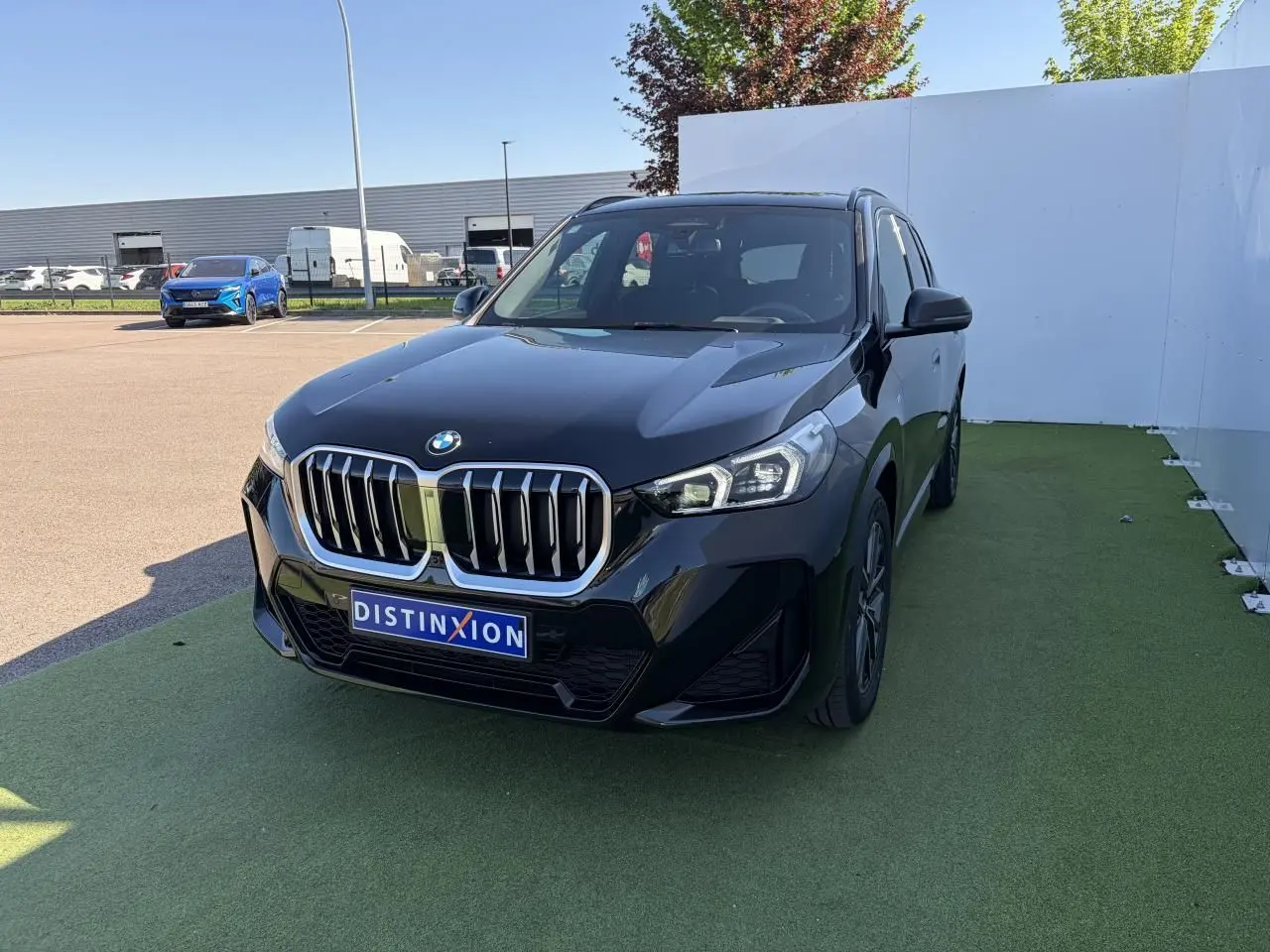 BMW X1 noir saphir vue 3/4 avant droite, calandre imposante et projecteurs LED sur parking extérieur.