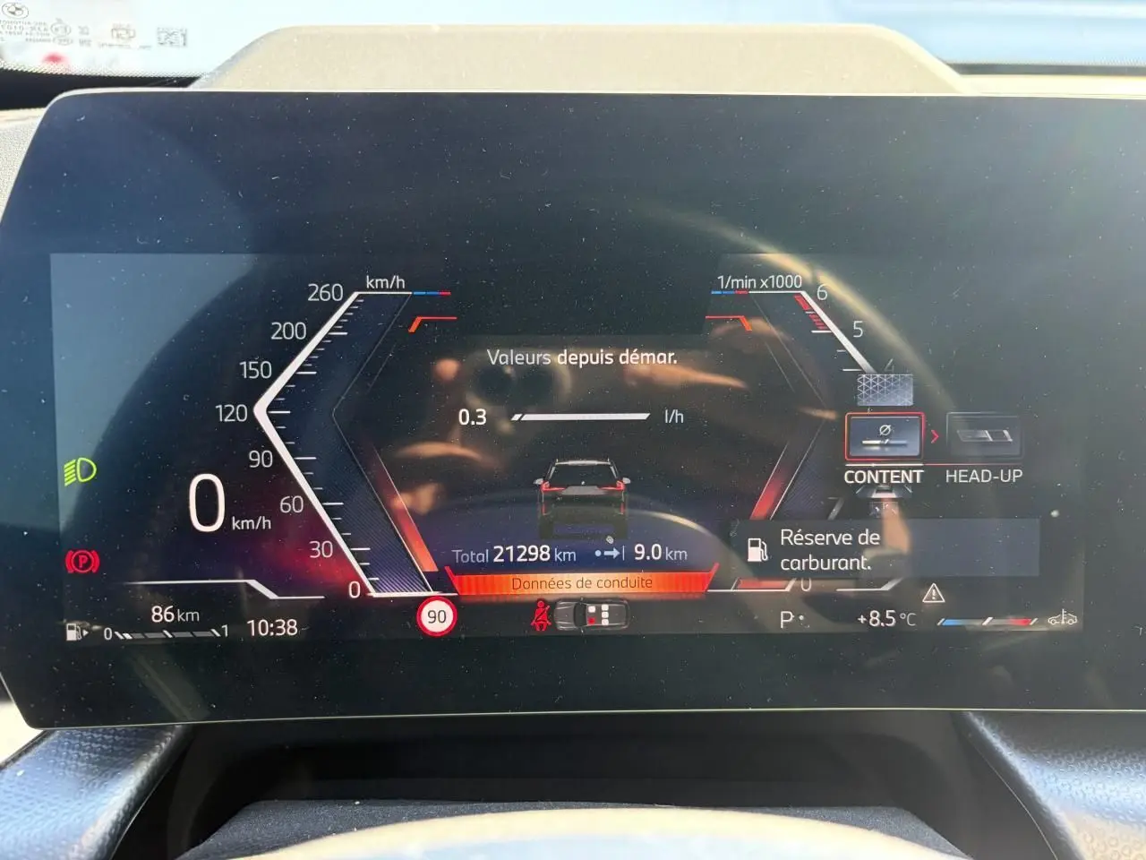 Affichage numérique du tableau de bord BMW X1 2025, montrant la consommation, vitesse 0 km/h et alerte réserve carburant.