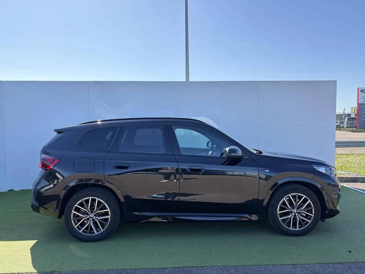 Profil droit d’un BMW X1 noir saphir 2025 avec jantes alliage 18 pouces et toit panoramique visible.