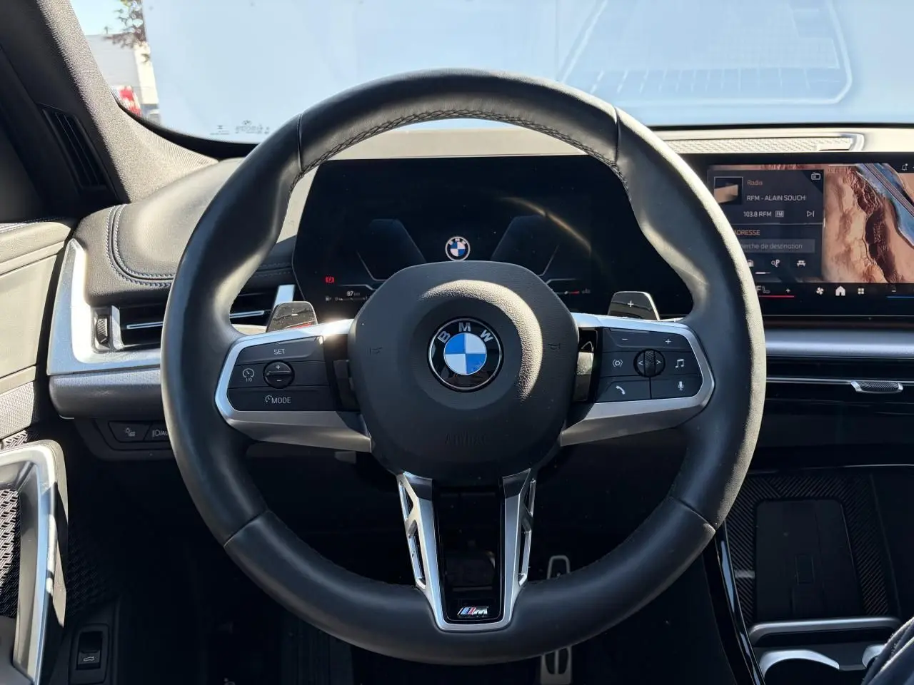 Vue frontale du volant cuir M noir avec commandes intégrées, tableau de bord numérique et écran tactile du BMW X1 noir Saphir 2025.