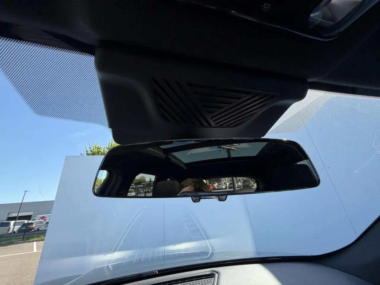 Vue intérieure centrée sur le rétroviseur intérieur et le toit ouvrant panoramique du BMW X1 noir Saphir 2025.