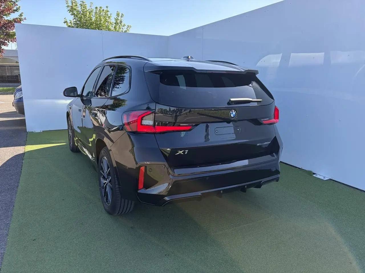 BMW X1 noir saphir vue 3/4 arrière droit, avec feux LED et vitres teintées sur fond extérieur clair.