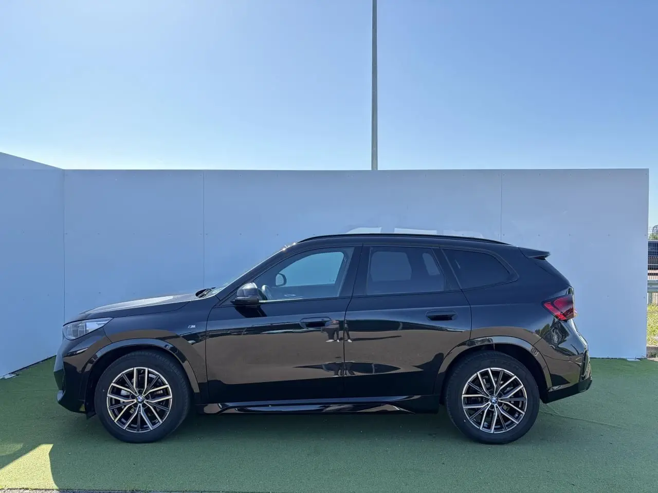 Profil côté gauche d’un BMW X1 noir saphir 2025 avec jantes alliage 18 pouces et toit panoramique visible.
