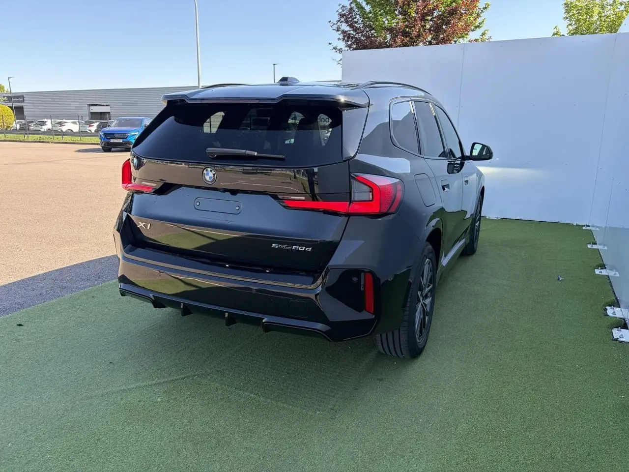 BMW X1 noir saphir vue 3/4 arrière droit, avec feux LED distinctifs et toit ouvrant panoramique visible.