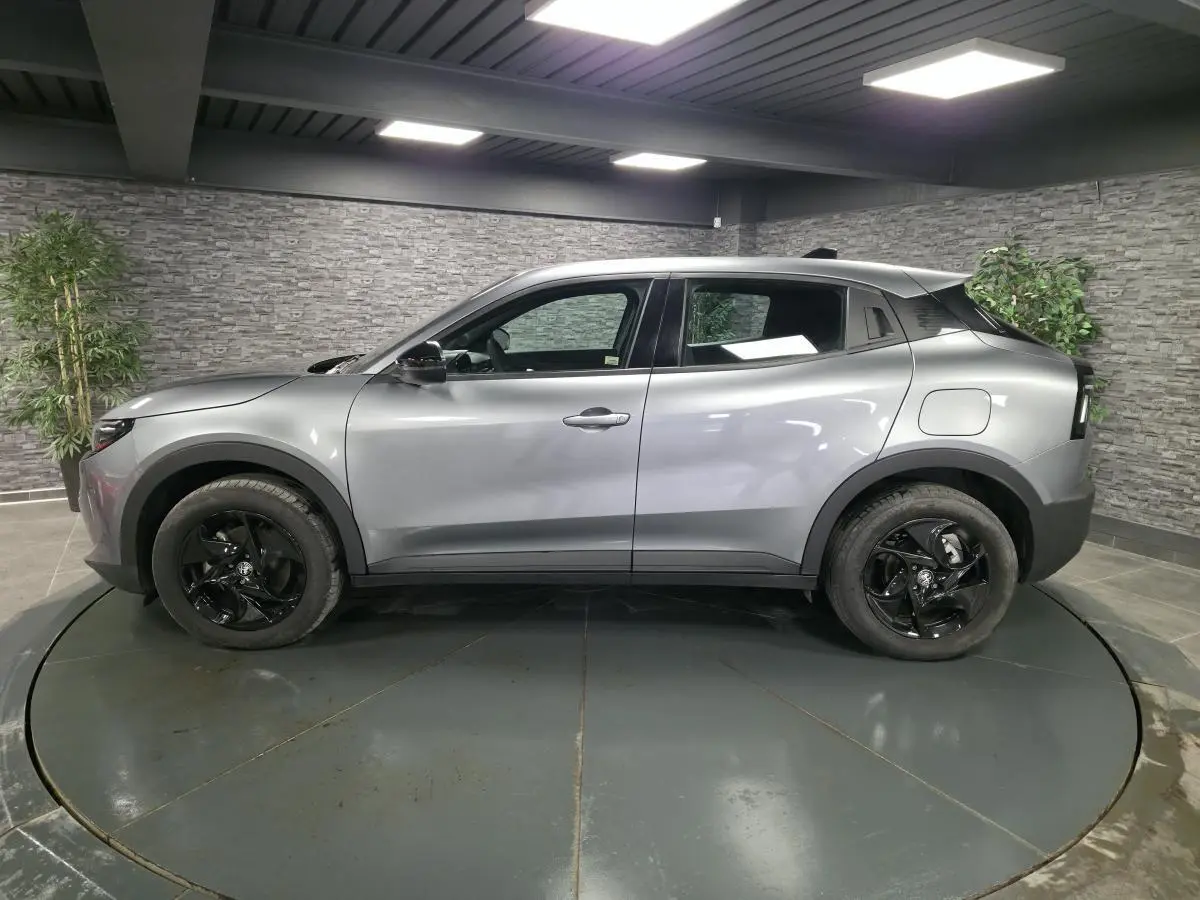 Vue de profil côté gauche d'une Alfa Romeo Junior 1.2 Ibrida gris métallisé avec jantes alliage noires dans un showroom.