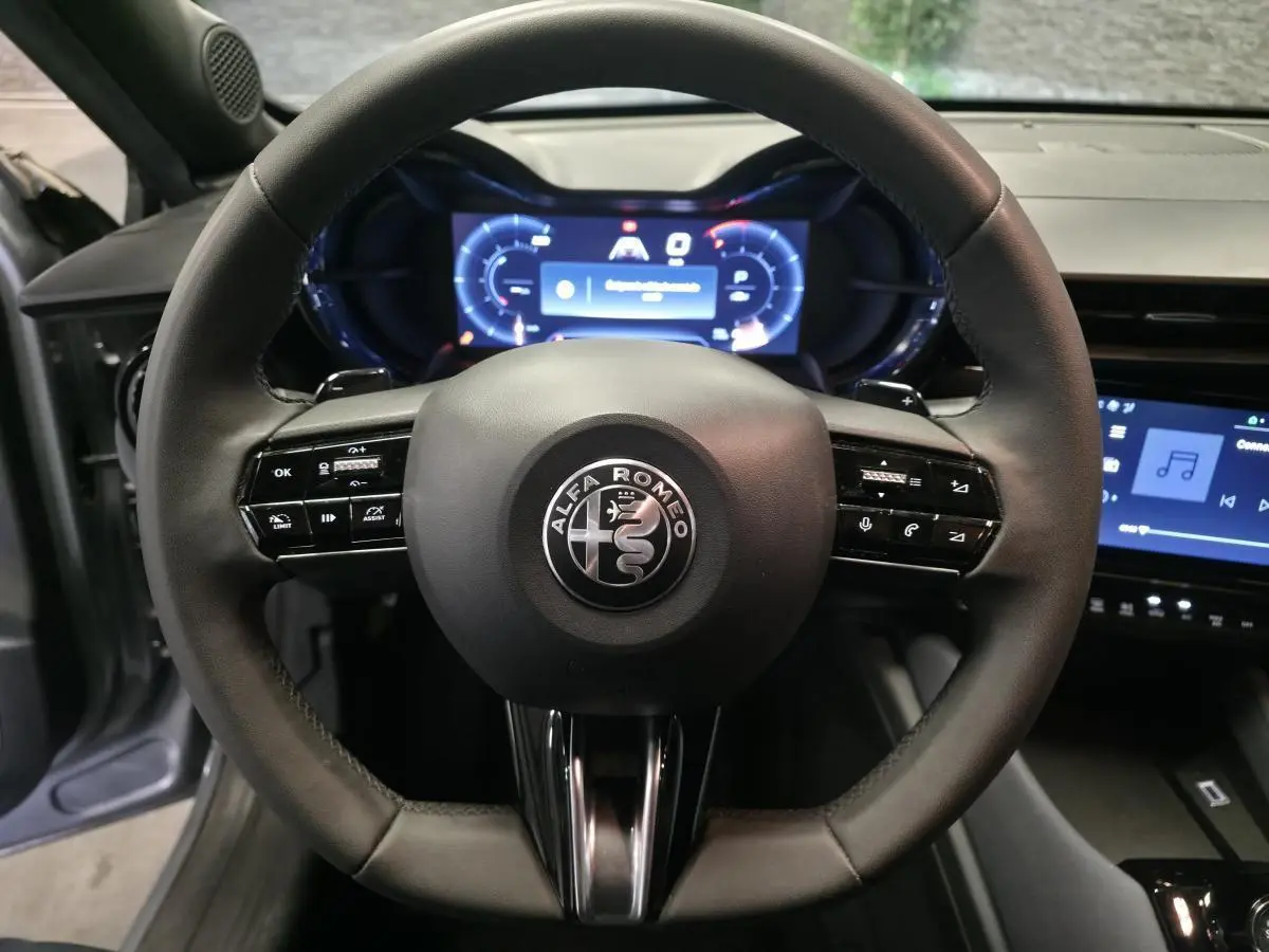 Vue rapprochée du volant noir multifonctions de l'Alfa Romeo Junior 2025 avec tableau de bord digital lumineux.