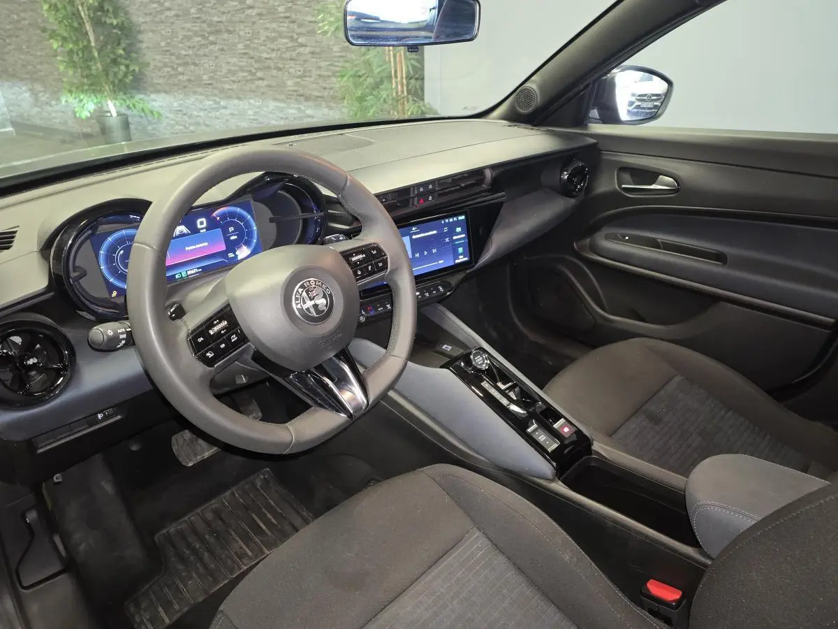 Vue intérieure côté conducteur de l'Alfa Romeo Junior 1.2 hybride 2025, avec tableau de bord digital et sellerie noire.